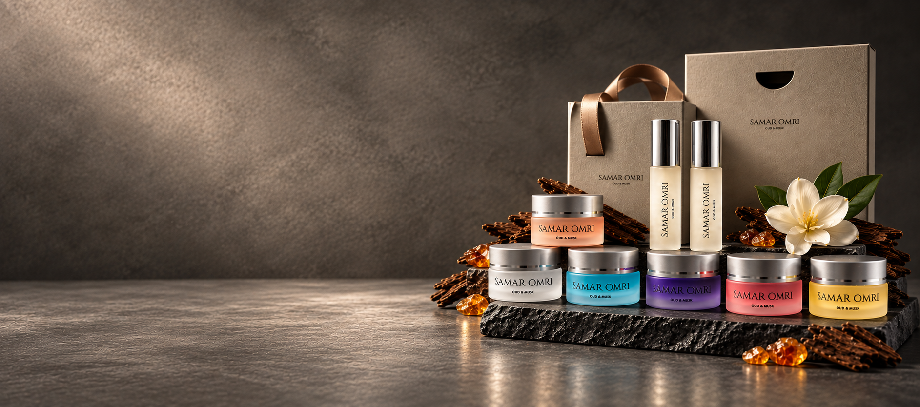 Samar Omri collection of perfume oil jars and rollers with gift packaging, oud wood and a white blossom on a dark stone backdrop